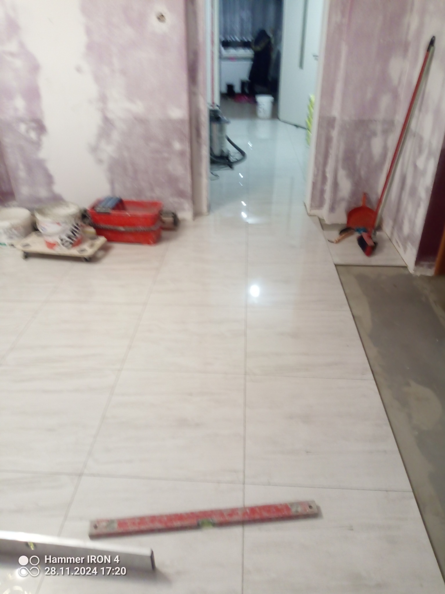 Ułożone jasne płytki podłogowe w trakcie prac wykończeniowych. Widoczne narzędzia glazurnicze i przygotowane ściany do malowania. Perspektywa z poziomu podłogi.