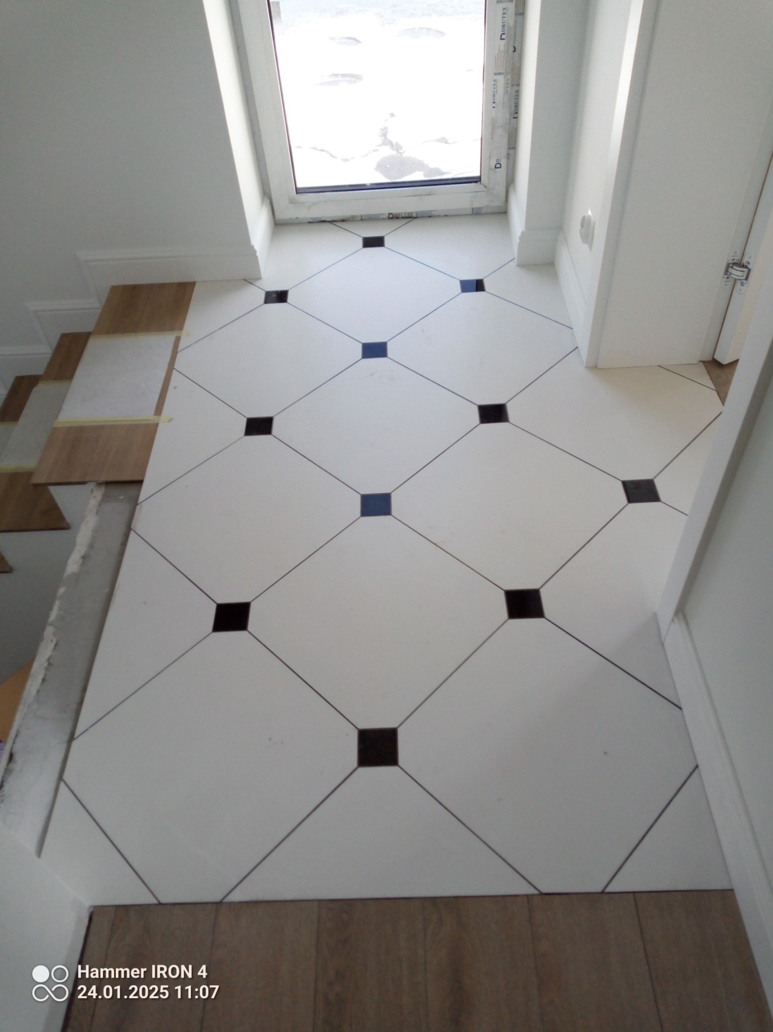 Białe płytki podłogowe z czarnymi akcentami ułożone w karo, widoczne przy oknie i drzwiach. Częściowo ułożona podłoga w Bargłówka.