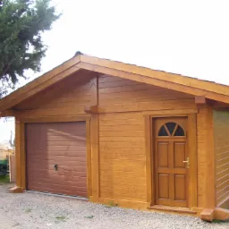 Drewniany budynek gospodarczy z bramą garażową i drzwiami wejściowymi, obok zaparkowana łódź na przyczepie.