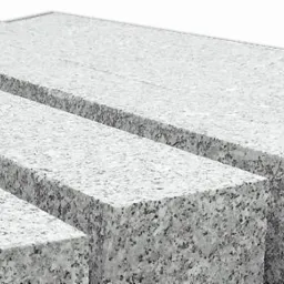 Szare kostki granitowe o surowej fakturze, ułożone obok siebie w różnych rozmiarach, z widocznymi nacięciami na jednej z nich.