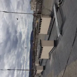 Czarny, bitumiczny dach z kominami wentylacyjnymi i antenami telewizyjnymi na tle pochmurnego nieba i zabudowy miejskiej.