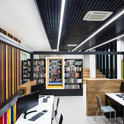 Piotrkurpaska photography - Wnętrze nowoczesnej biblioteki z regałami pełnymi książek, stanowiskami komputerowymi i elementami dekoracyjnymi w postaci kolorowych pionowych pasków.