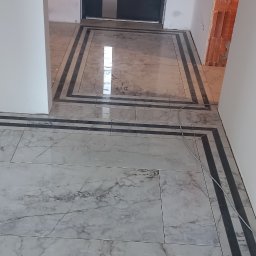 Wintech - Ułożona marmurowa podłoga z dekoracyjnymi czarnymi paskami w korytarzu, widoczne niedokończone ściany i instalacja elektryczna.
