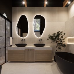 TULLAHOME Sp. z o.o. - Nowoczesna łazienka z dwoma czarnymi umywalkami w kształcie mis, podświetlanymi lustrami o organicznym kształcie, drewnianą szafką pod umywalką, kabiną prysznicową ze szkła ornamentowego...