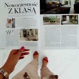 TULLAHOME Sp. z o.o. - Otwarta gazeta z artykułem o aranżacji wnętrz, prezentująca zdjęcia nowoczesnych domów. Widoczne nogi osoby trzymającej gazetę, marmurowa podłoga.