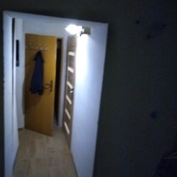 Mariusz Kujawski M-BUD - Korytarz po remoncie: świeżo pomalowane ściany w odcieniach szarości, jasna podłoga, widoczne drzwi wejściowe i wewnętrzne. Oświetlenie sufitowe.