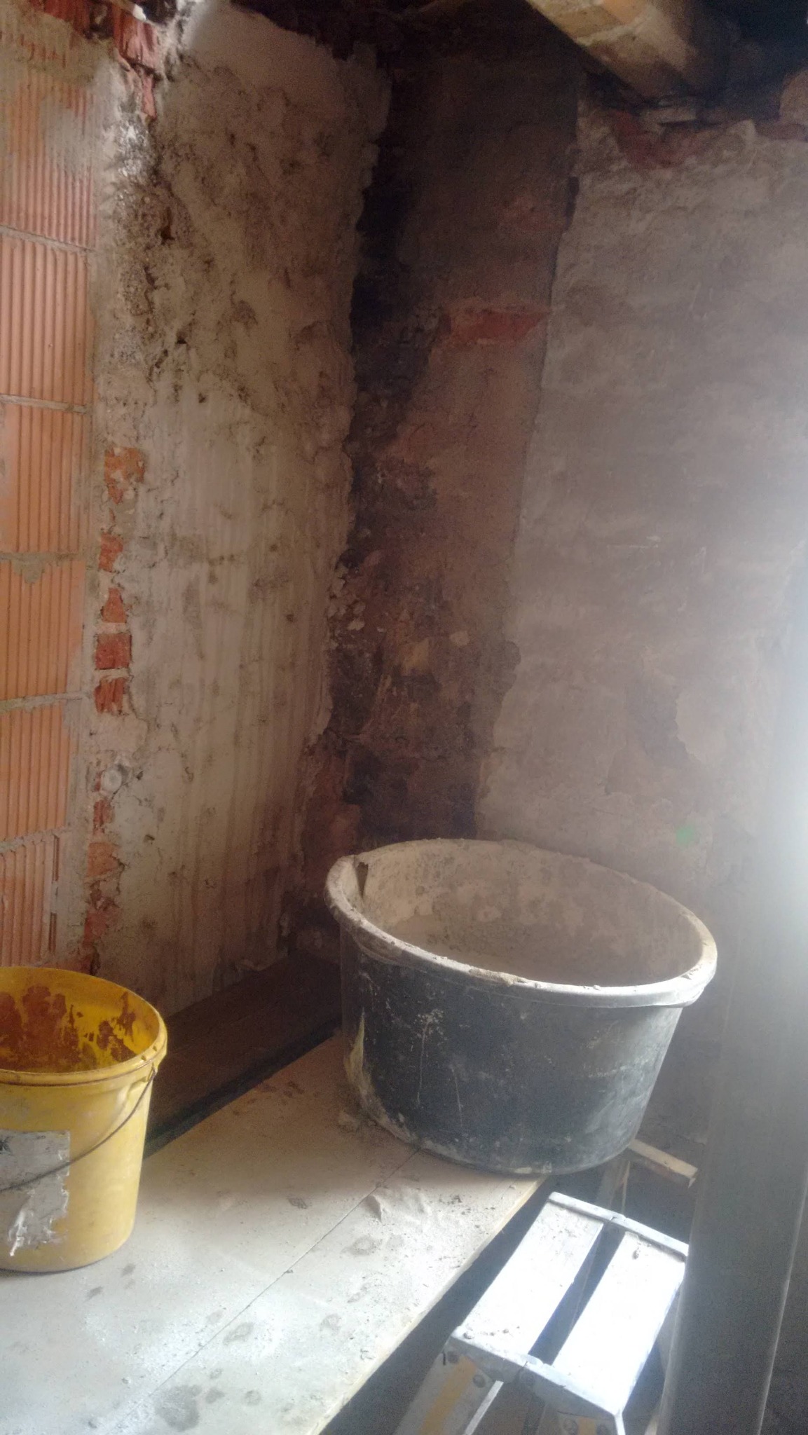 Ściana w trakcie prac przygotowawczych z widocznymi warstwami muru i nałożonym tynkiem, obok stoją wiadra z zaprawą, co sugeruje etap prac remontowych.