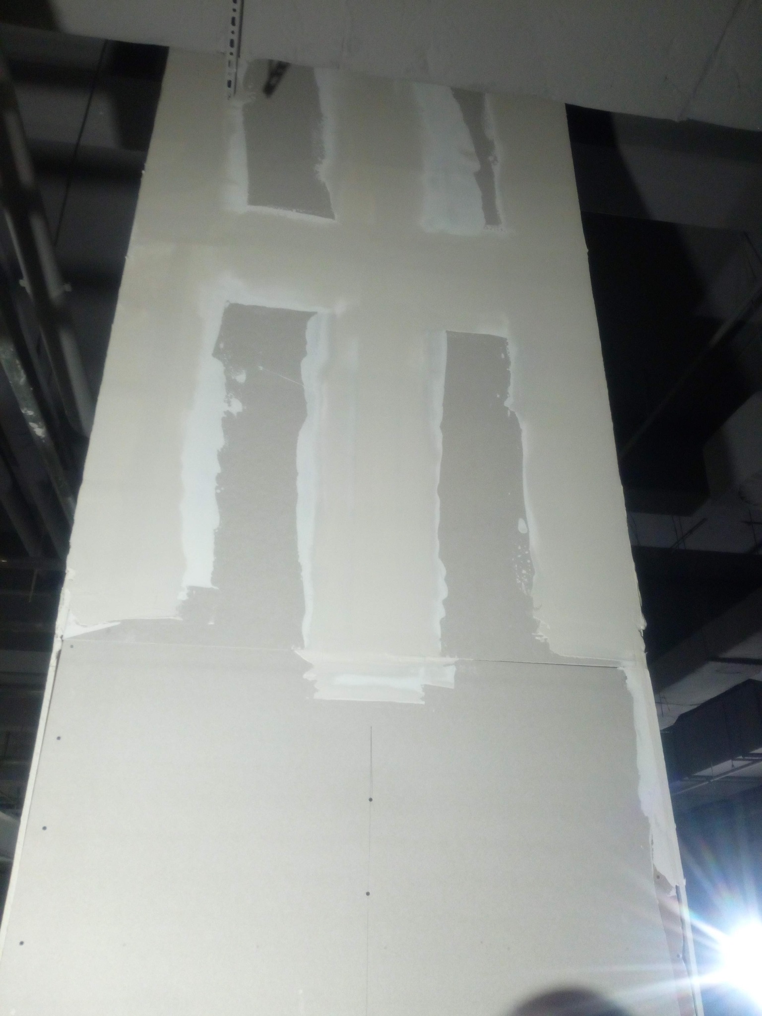 Płyta gipsowa z nałożoną warstwą szpachli w czterech miejscach, widok z dołu, surowe wykończenie, oświetlenie budowlane.