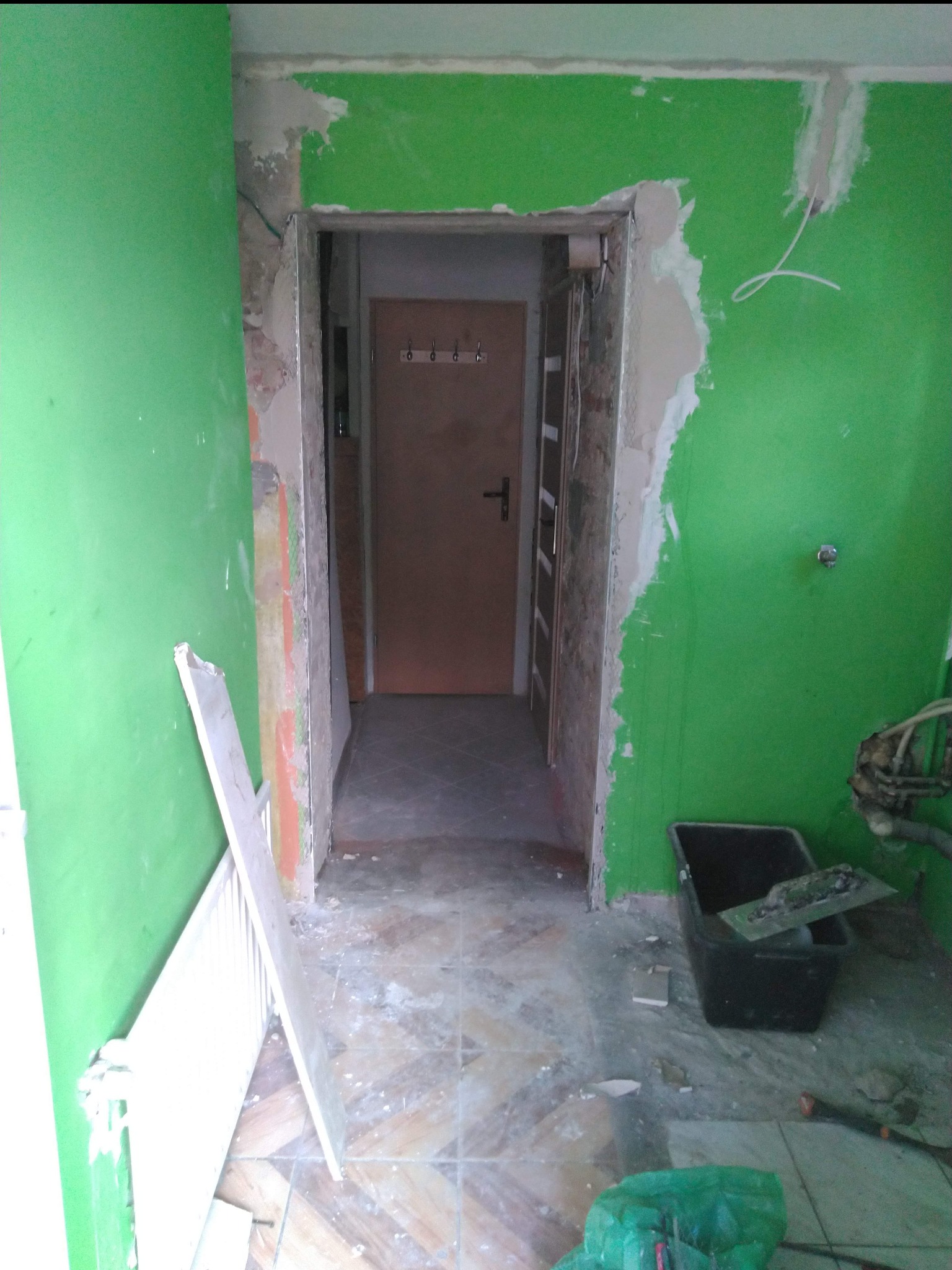 Pokój w trakcie prac przygotowawczych: zielone ściany z fragmentami gładzi, widoczne narzędzia i materiały budowlane, przygotowanie do dalszych prac wykończeniowych.