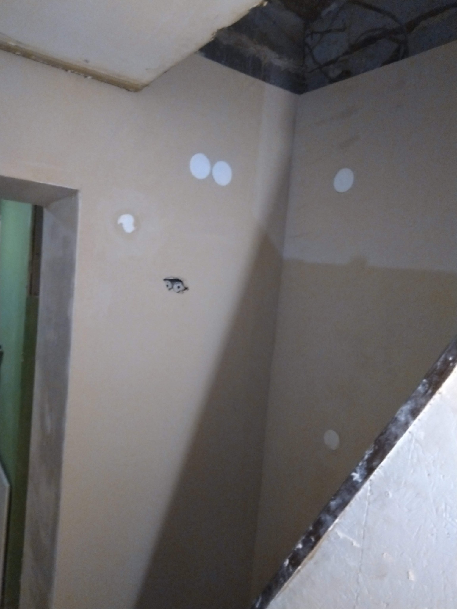 Ściana po nałożeniu gładzi, z widocznymi otworami na gniazdka i zabezpieczonymi punktami świetlnymi. Fragment schodów w prawym dolnym rogu kadru.