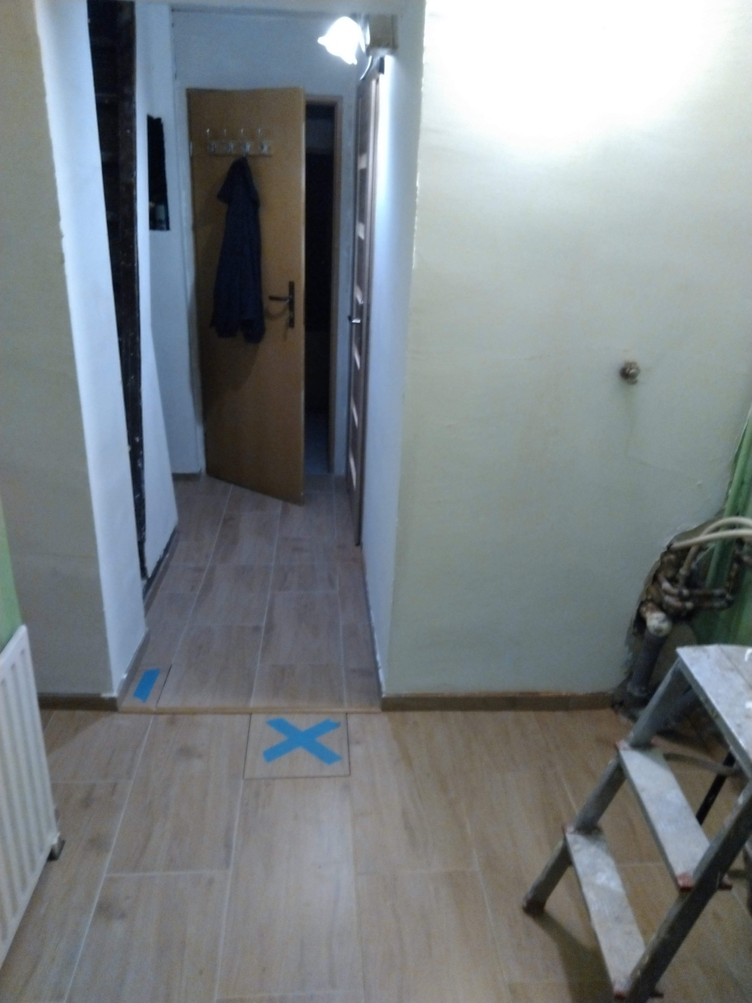 Korytarz w trakcie prac: położone płytki podłogowe, ściany przygotowane do prac wykończeniowych, widoczna drabina malarska i instalacja. Otwarta drewniana futryna.