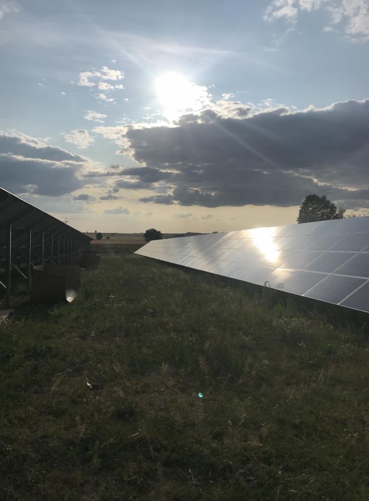 Instalacja paneli słonecznych na łące, widoczne kartony po panelach, słońce odbija się w panelach.