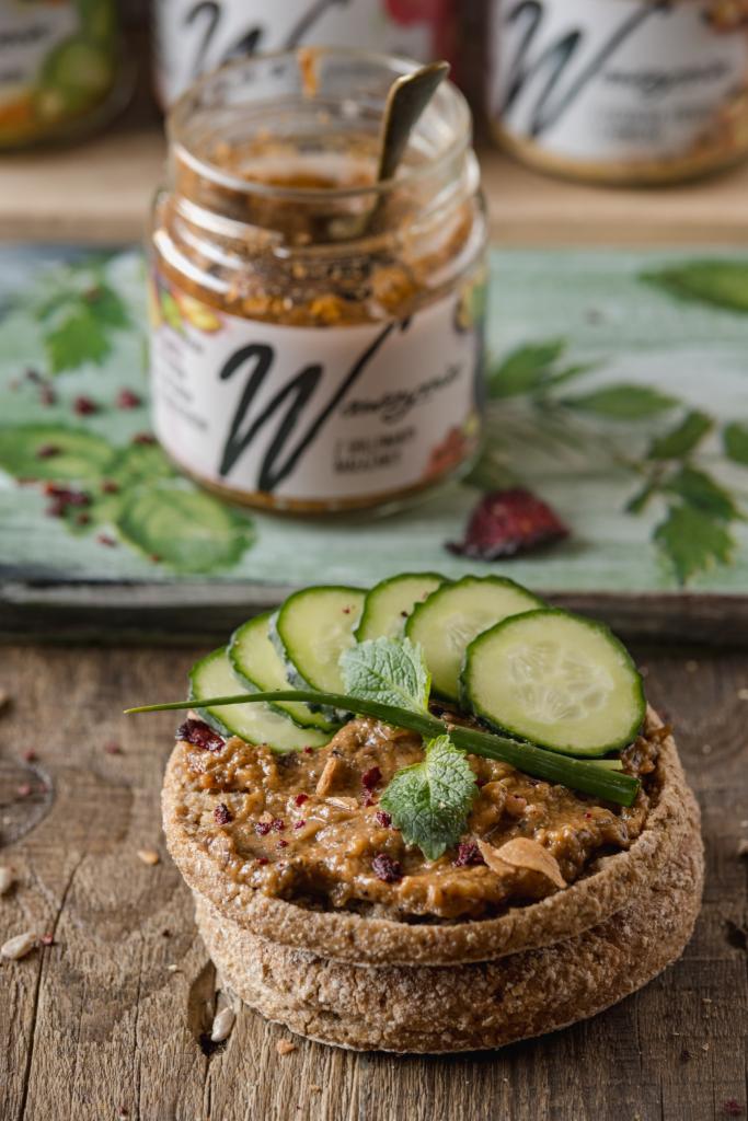 Kanapka z pastą, ogórkiem i miętą na drewnianym stole, w tle słoik z pastą marki W.