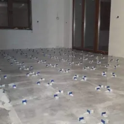 Układanie szarych płytek podłogowych z systemem poziomowania płytek w jasnym pokoju z oknem i drzwiami balkonowymi.