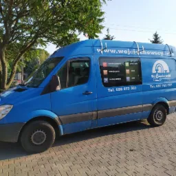 Niebieski samochód dostawczy z reklamą firmy instalacyjnej Wojciechowski, prezentujący zakres usług: centralne ogrzewanie, pompy ciepła, instalacje gazowe, solarne, sanitarne i klimatyzacja...