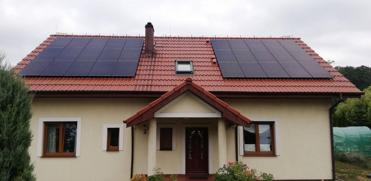 Dom jednorodzinny z panelami słonecznymi na czerwonym dachu, widok z przodu, pochmurne niebo.