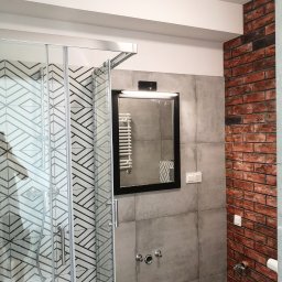 Venkonsv - Nowoczesna łazienka w Warszawie po remoncie: kabina prysznicowa z geometrycznym wzorem na płytkach, lustro w czarnej ramie z oświetleniem, ściana wyłożona płytkami imitującymi czerwoną cegłę.