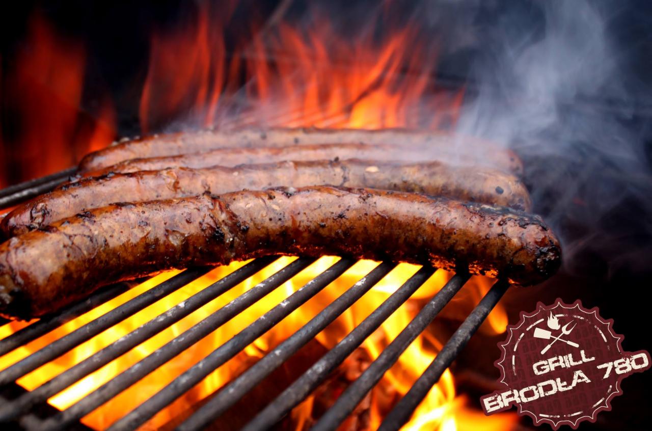 Soczyste, brązowe kiełbaski grillowane na ruszcie, otoczone płomieniami ognia, z logo 'Grill Broda 780' w prawym dolnym rogu.