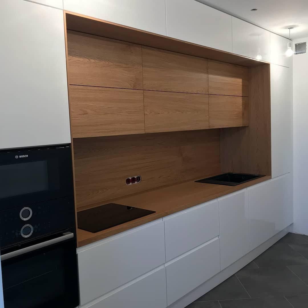 Nowoczesna kuchnia: białe szafki dolne i górne z drewnianymi frontami, czarna płyta grzewcza i zlewozmywak, piekarnik Bosch po lewej stronie.