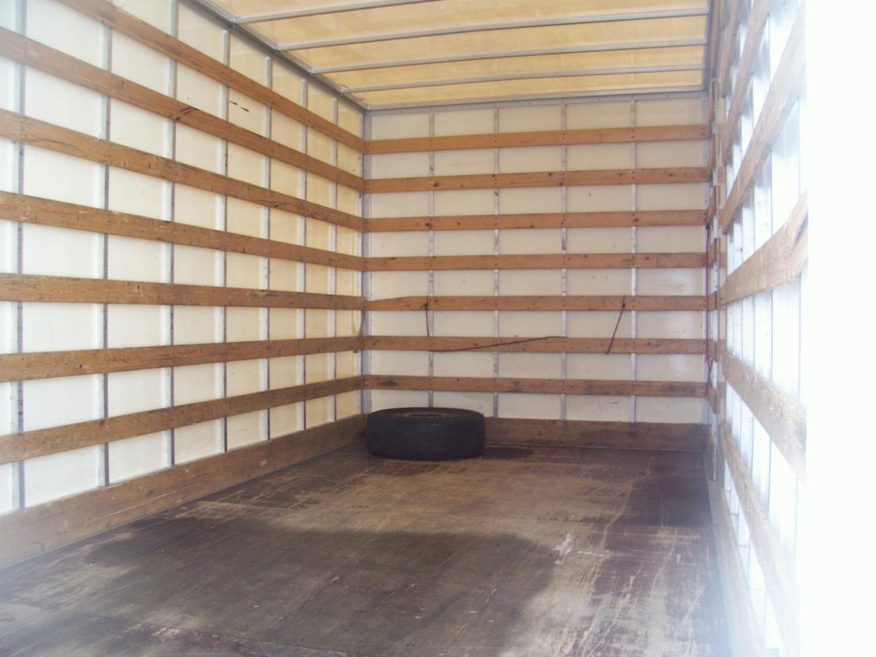 Wnętrze pustej przestrzeni ładunkowej busa z drewnianymi listwami zabezpieczającymi i pojedynczą oponą na podłodze.