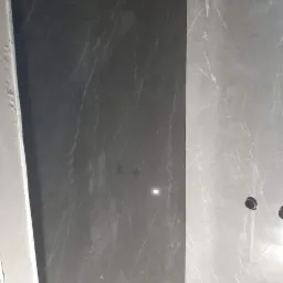 Ściana wyłożona płytkami imitującymi marmur w odcieniach szarości, widoczne otwory na gniazdka elektryczne.