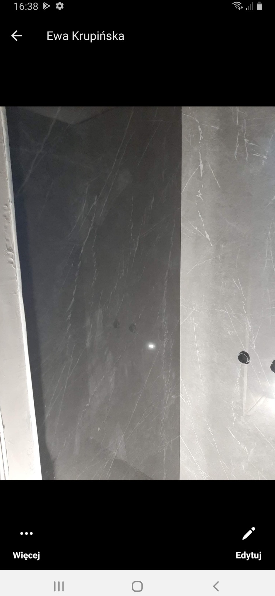 Ściana wyłożona płytkami imitującymi marmur w odcieniach szarości, widoczne otwory na gniazdka elektryczne.