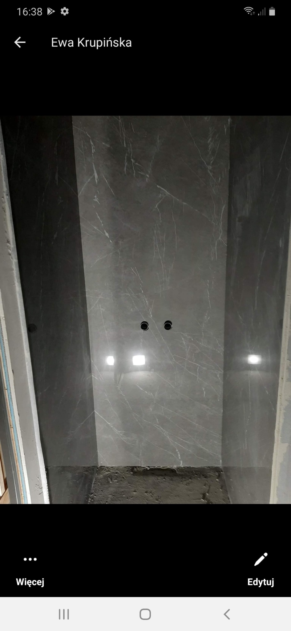 Ściana wyłożona szarymi płytkami imitującymi marmur, z widocznymi otworami na punkty świetlne, w trakcie prac wykończeniowych.