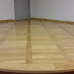 Parkiet dębowy ułożony w kwadraty z paskami, po cyklinowaniu i lakierowaniu, widoczny połysk i gładka powierzchnia, przy ścianie listwa przypodłogowa.