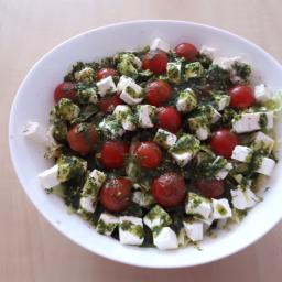 Stowarzyszenie Na Rzecz Rozwoju Gminy Gać - Sałatka z pomidorków koktajlowych, sera feta w kostkach i zielonego pesto, podana w białej misce na drewnianym stole.