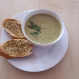 Stowarzyszenie Na Rzecz Rozwoju Gminy Gać - Kremowa zupa w białej miseczce, udekorowana gałązką kopru, podana z dwoma kromkami chleba czosnkowego na białym talerzu.