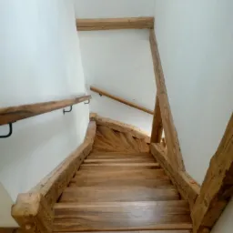 Spiralne schody z jasnego drewna z surowymi belkami konstrukcyjnymi, widok z góry na dół, minimalistyczne wnętrze z białymi ścianami.