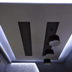 Nowoczesny sufit podwieszany z oświetleniem LED wzdłuż krawędzi i czarnymi lampami wiszącymi na tle dekoracyjnej ściany z falistym wzorem.