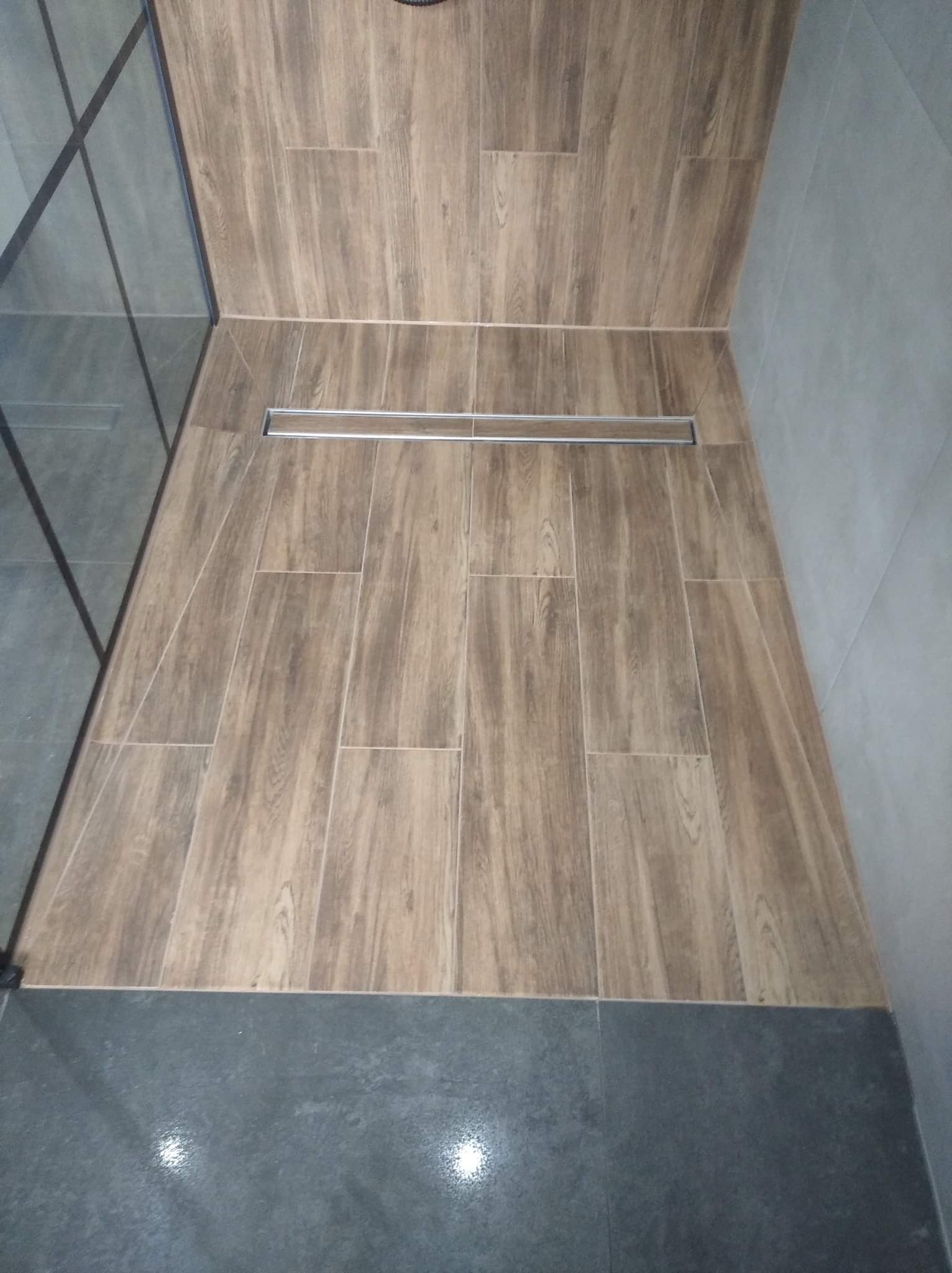 Wykończona podłoga prysznica z drewnopodobnych płytek ceramicznych i odpływem liniowym, widok z góry.