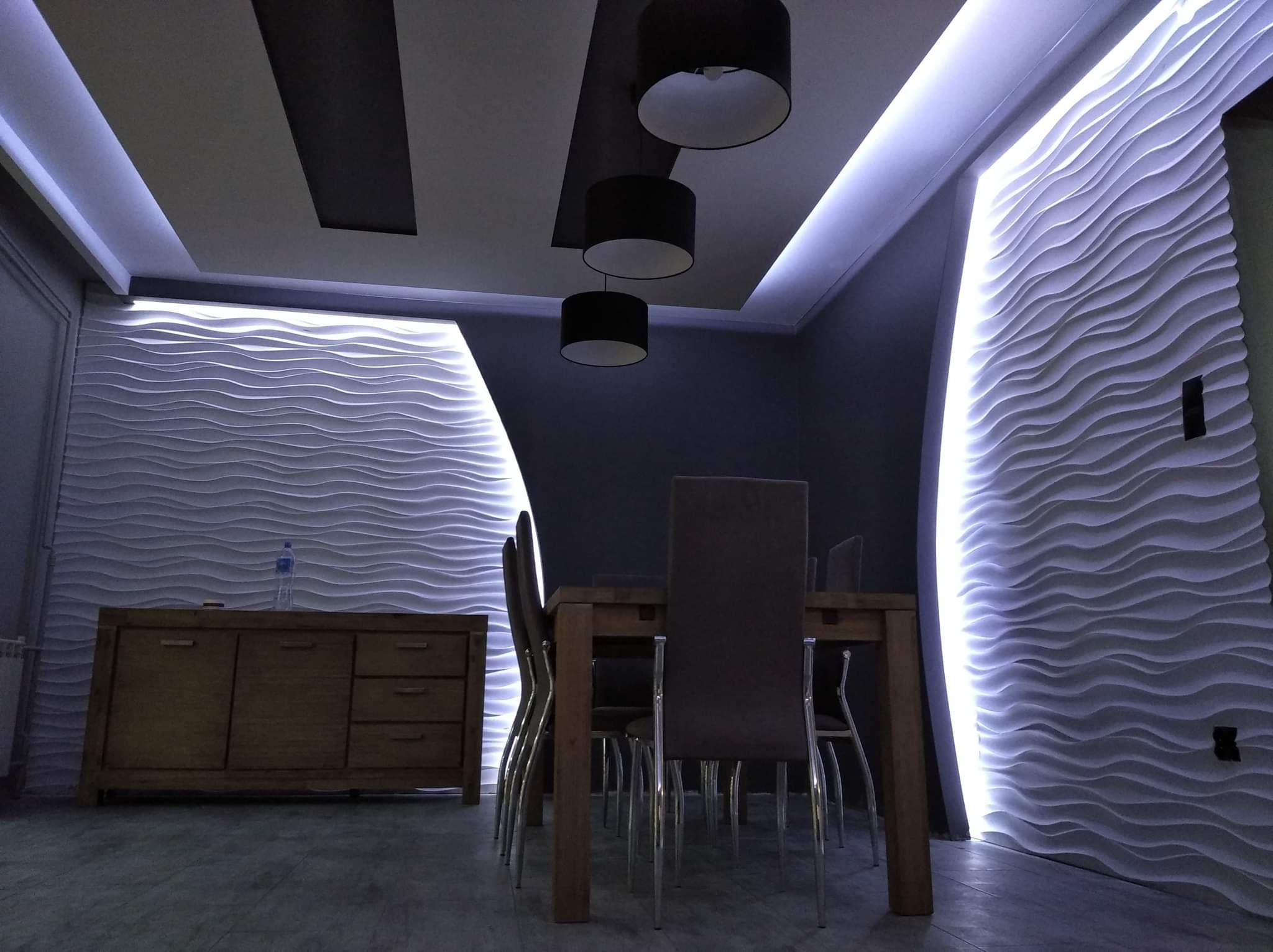 Jadalnia z podświetlanymi panelami ściennymi 3D o falistym wzorze, nowoczesne lampy wiszące i drewniany kredens