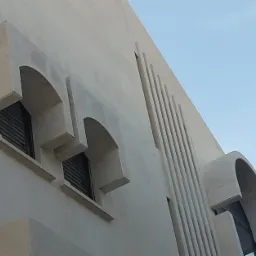 Elewacja budynku z łukowymi oknami i pionowymi zdobieniami w odcieniach bieli, widziana pod kątem z dołu na tle błękitnego nieba.