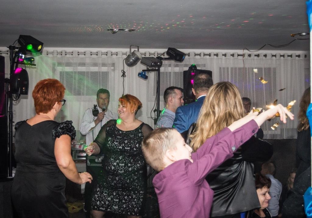 Rozbawieni goście tańczą na parkiecie podczas imprezy z DJ-em, w tle oświetlenie dyskotekowe i konfetti w powietrzu.