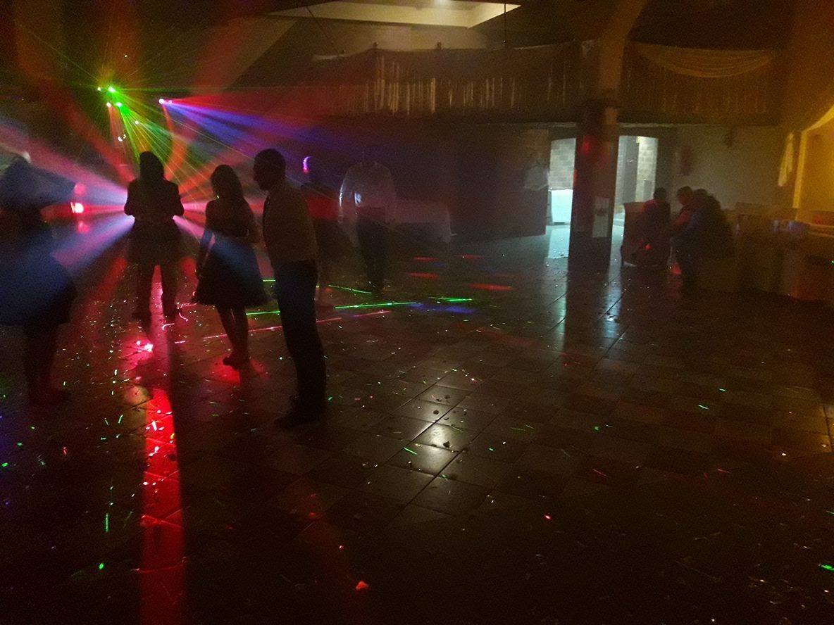 Parkiet w konfetti oświetlony laserami podczas imprezy. W tle sylwetki tańczących osób i elementy wystroju sali.