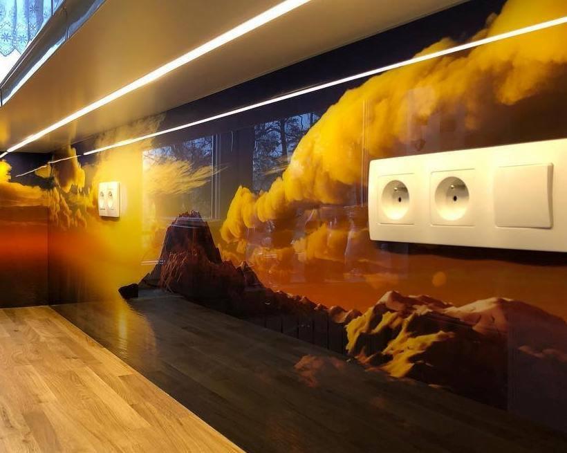 Szklana ściana w kuchni z nadrukowanym krajobrazem górskim o zachodzie słońca, gniazdka elektryczne i drewniany blat