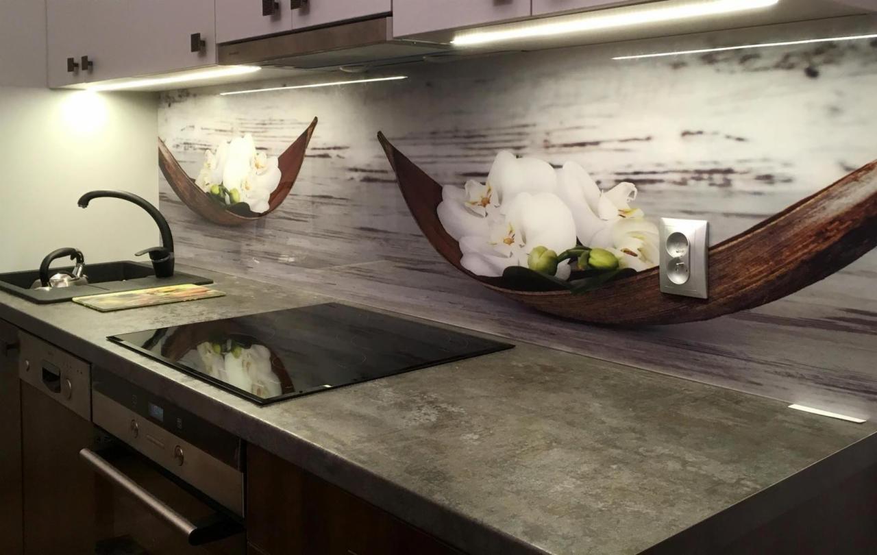 Szklana ściana nad blatem kuchennym z motywem orchidei w drewnianej łodzi, oświetlenie LED pod szafkami.