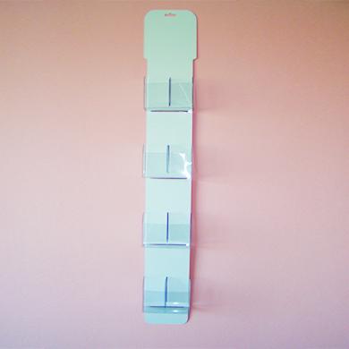 Pionowy, czteropoziomowy stojak na ulotki z przezroczystymi kieszeniami, zamontowany na różowej ścianie.