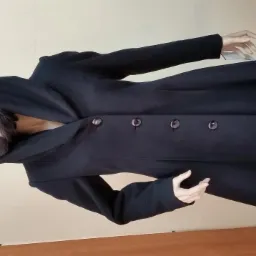 Czarny, wełniany płaszcz z kapturem, zapinany na cztery guziki, prezentowany na manekinie z peruką.