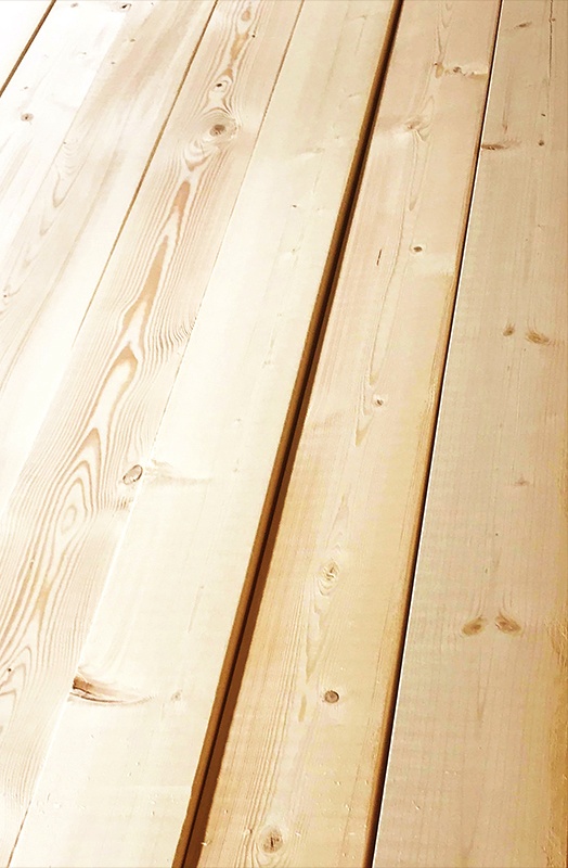 Stos jasnej tarcicy budowlanej z wyraźnym rysunkiem słojów, ułożonej pod kątem.