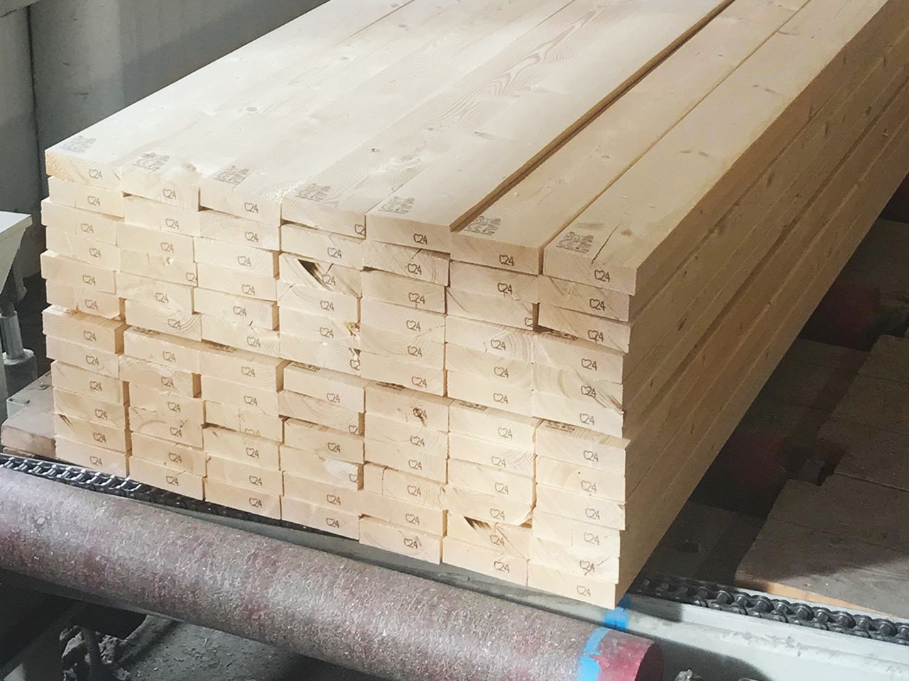 Stos tarcicy budowlanej C24 ułożony na metalowym transporterze w hali produkcyjnej, widoczne oznaczenia na każdym elemencie.