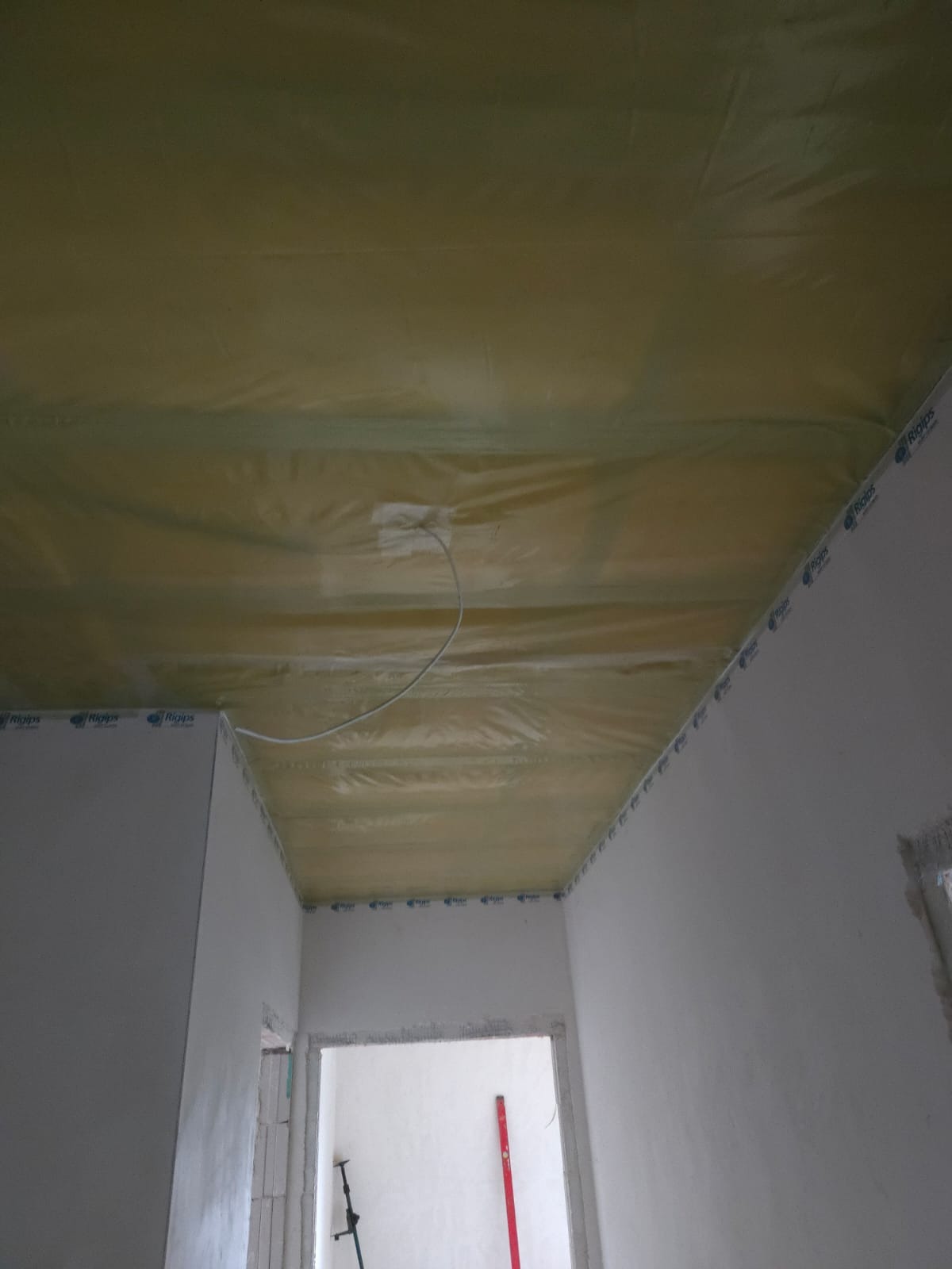 Sufit podwieszany z płyt gipsowo-kartonowych w trakcie montażu, widoczne profile i folia paroizolacyjna, przewody elektryczne. Ściany w surowym tynku.