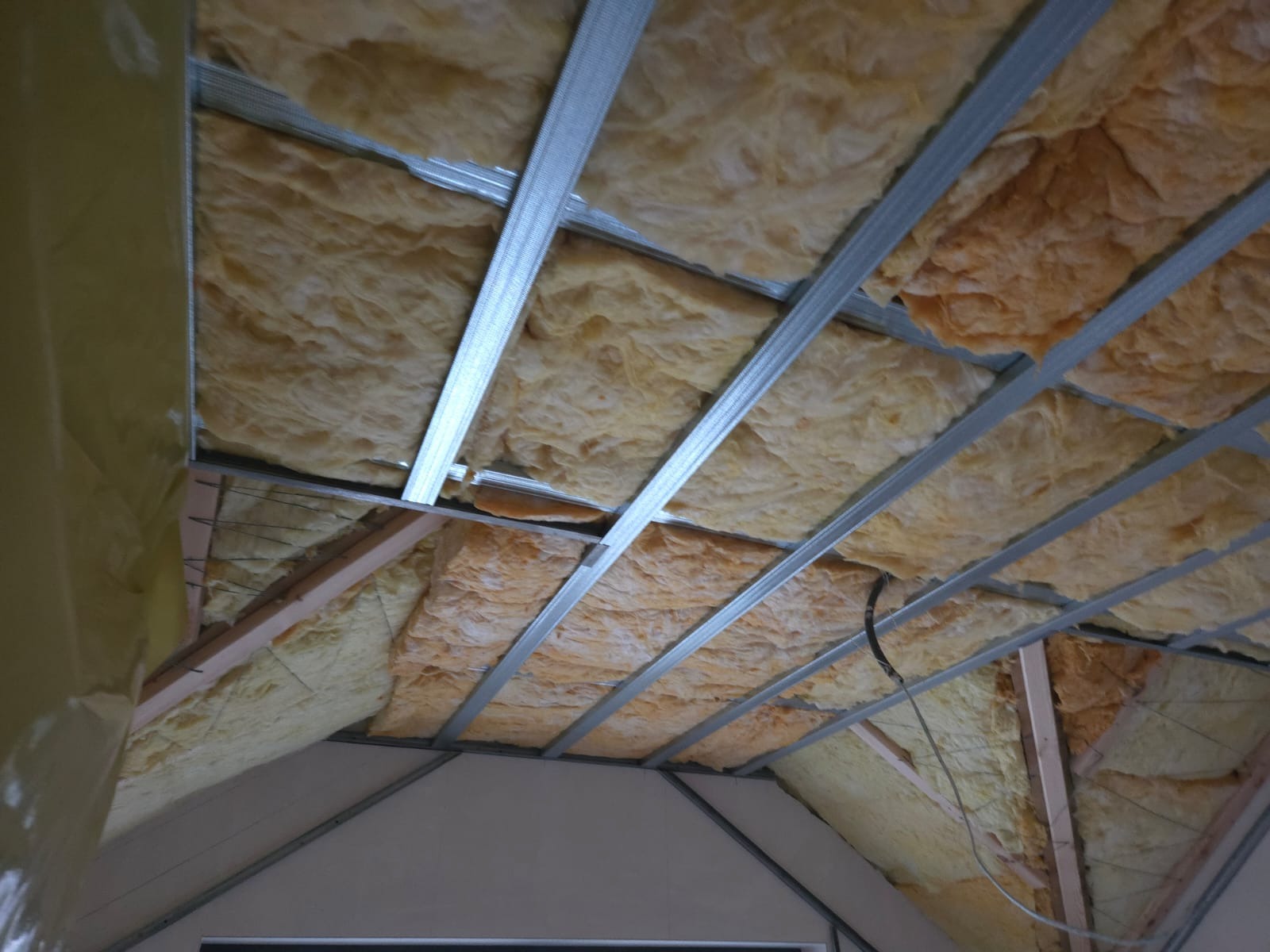 Ocieplenie poddasza wełną mineralną, widoczne metalowe profile konstrukcyjne i drewniane elementy więźby dachowej. Prace wykończeniowe w trakcie realizacji.