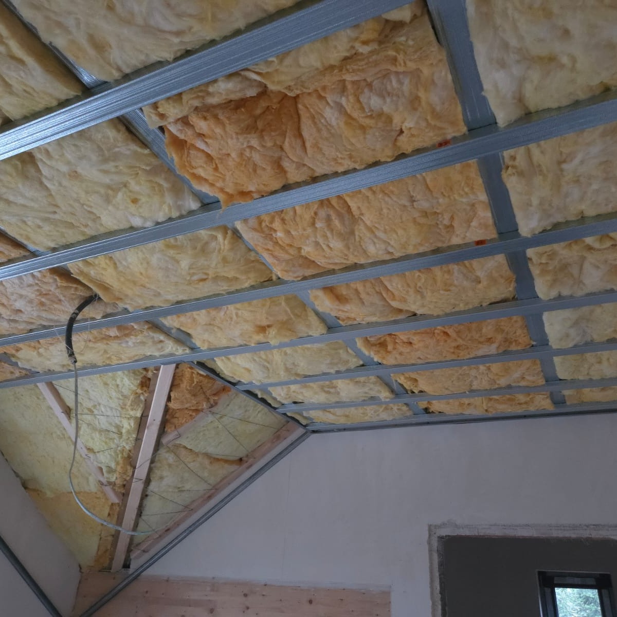 Ocieplenie poddasza wełną mineralną, widoczne metalowe profile konstrukcyjne. Ukończony etap prac przed zakryciem płytami gipsowymi. Widok z dołu.