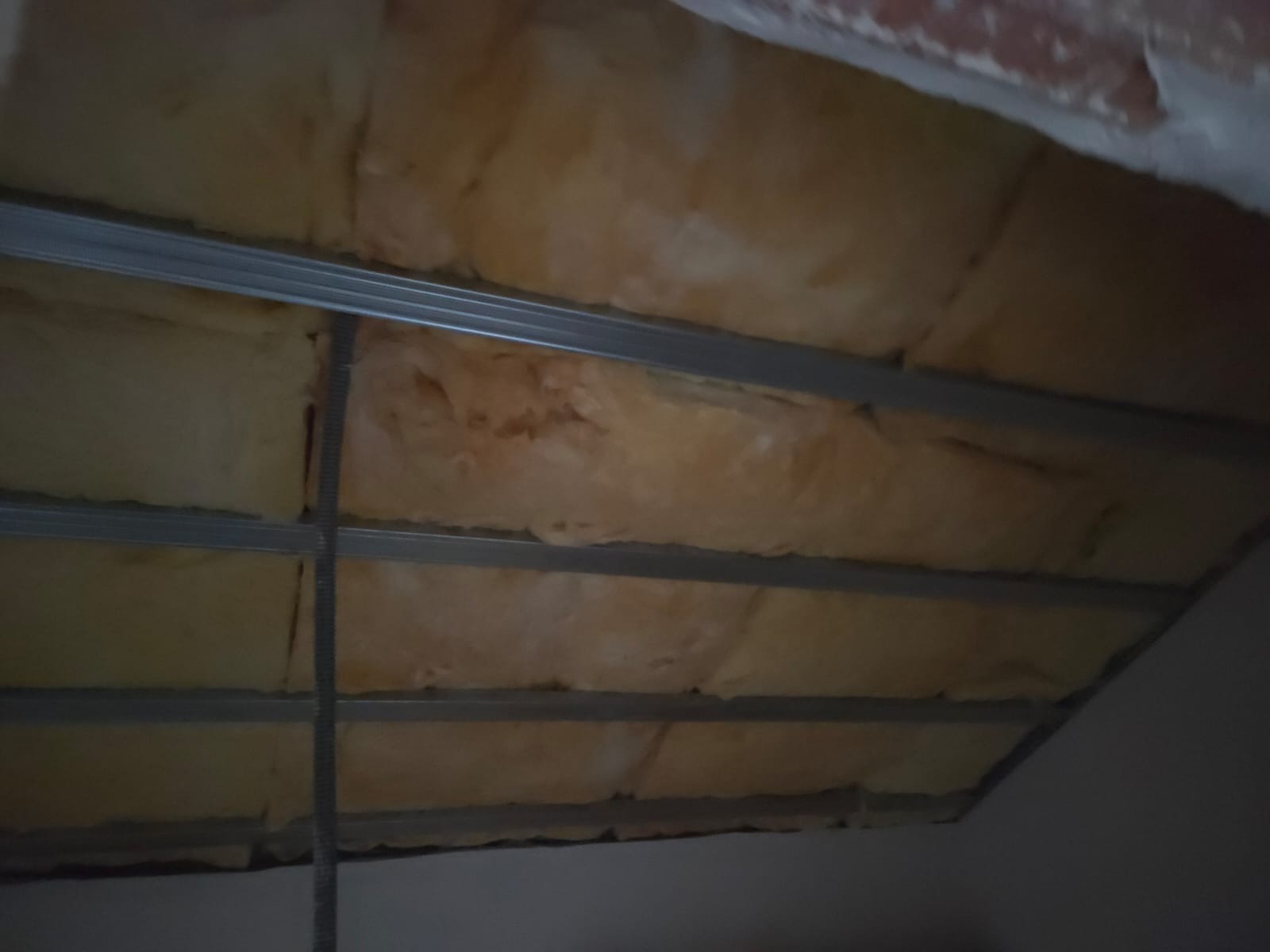 Ocieplenie poddasza wełną mineralną, widoczne metalowe profile konstrukcyjne. Izolacja termiczna w trakcie montażu, sufit podwieszany w budowie.