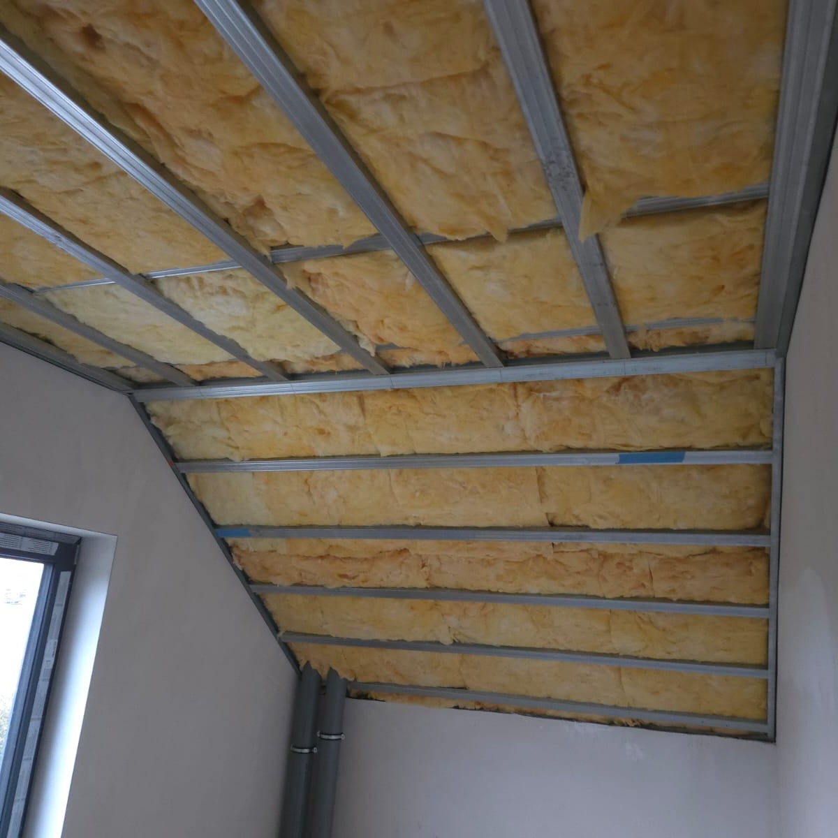 Ocieplenie poddasza wełną mineralną w Goleniowie. Widoczne metalowe profile konstrukcyjne i izolacja termiczna. Prace wykończeniowe w trakcie realizacji.