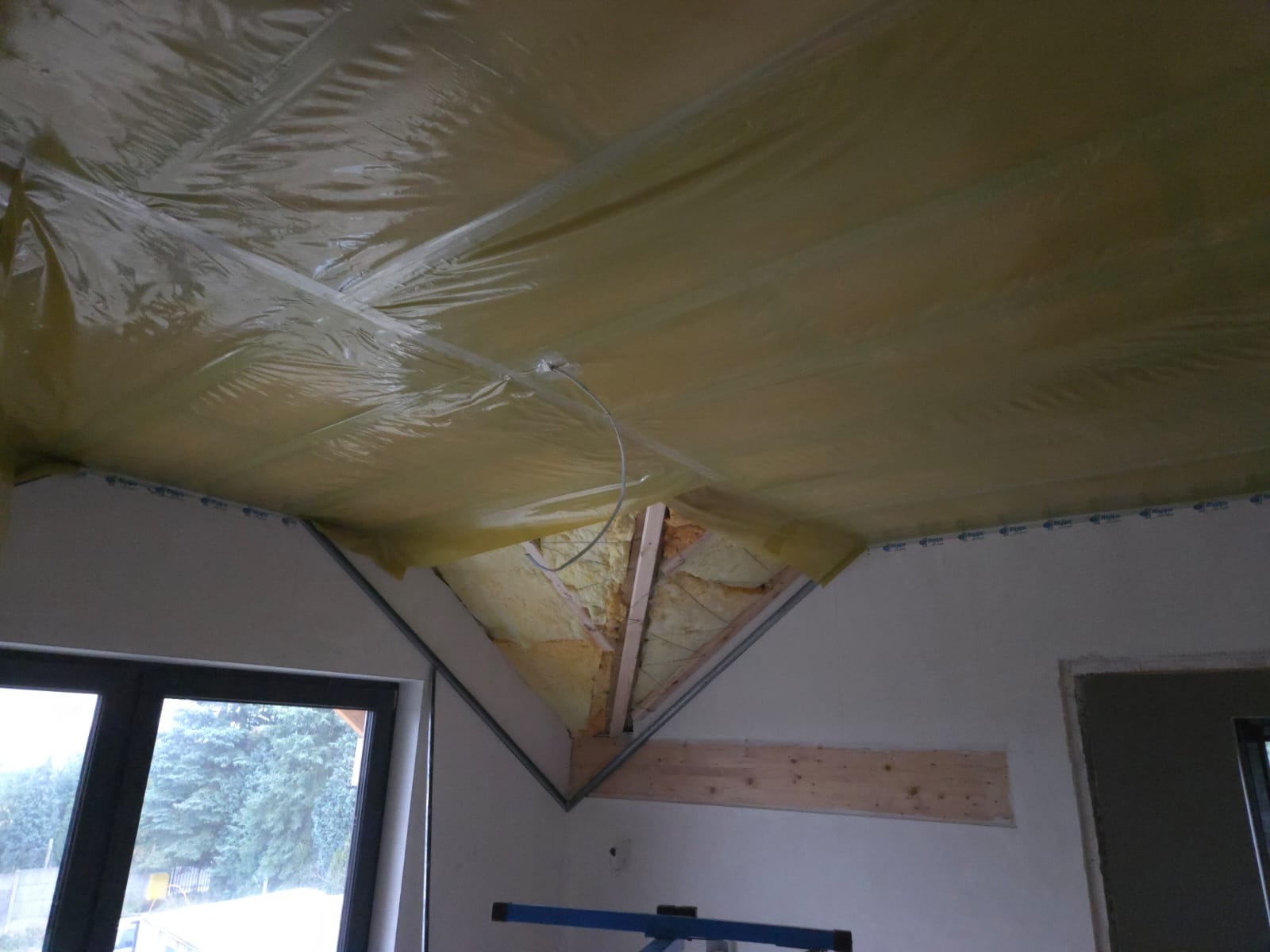 Ocieplenie poddasza wełną mineralną, zabezpieczone folią paroizolacyjną. Widoczne elementy konstrukcji dachu i okno. Prace wykończeniowe w trakcie realizacji.