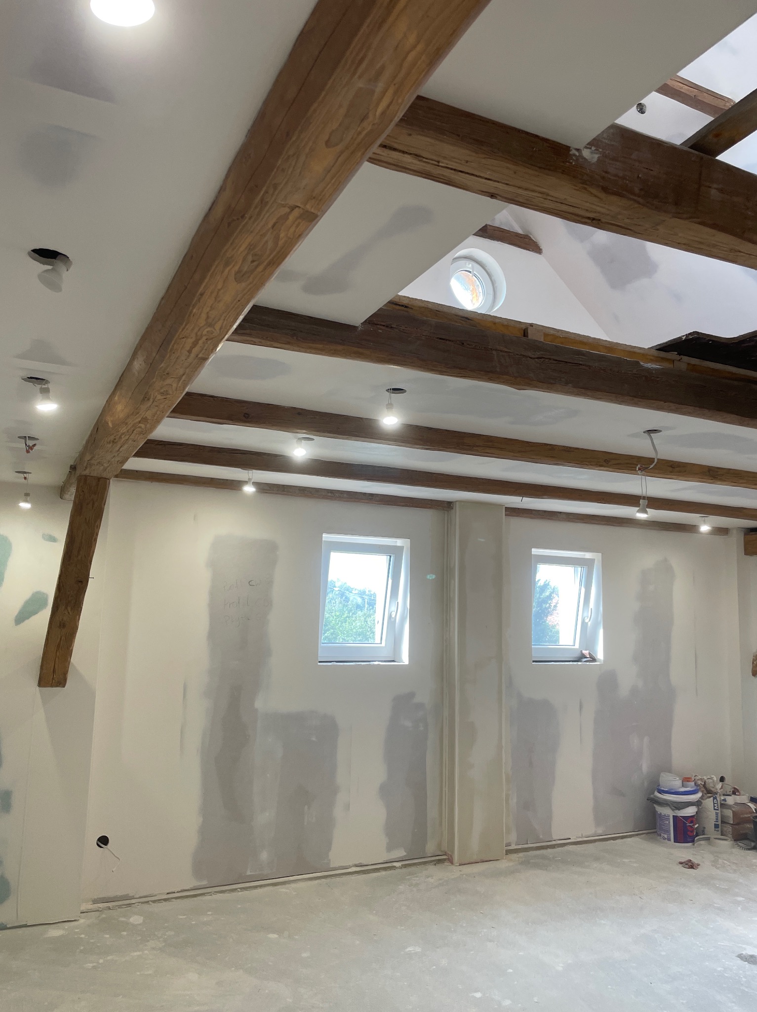 Wnętrze poddasza z drewnianą konstrukcją stropu, wykończone ściany przygotowane do malowania, widoczne ślady po szpachlowaniu i gładziowaniu, okna dachowe i oświetlenie punktowe.